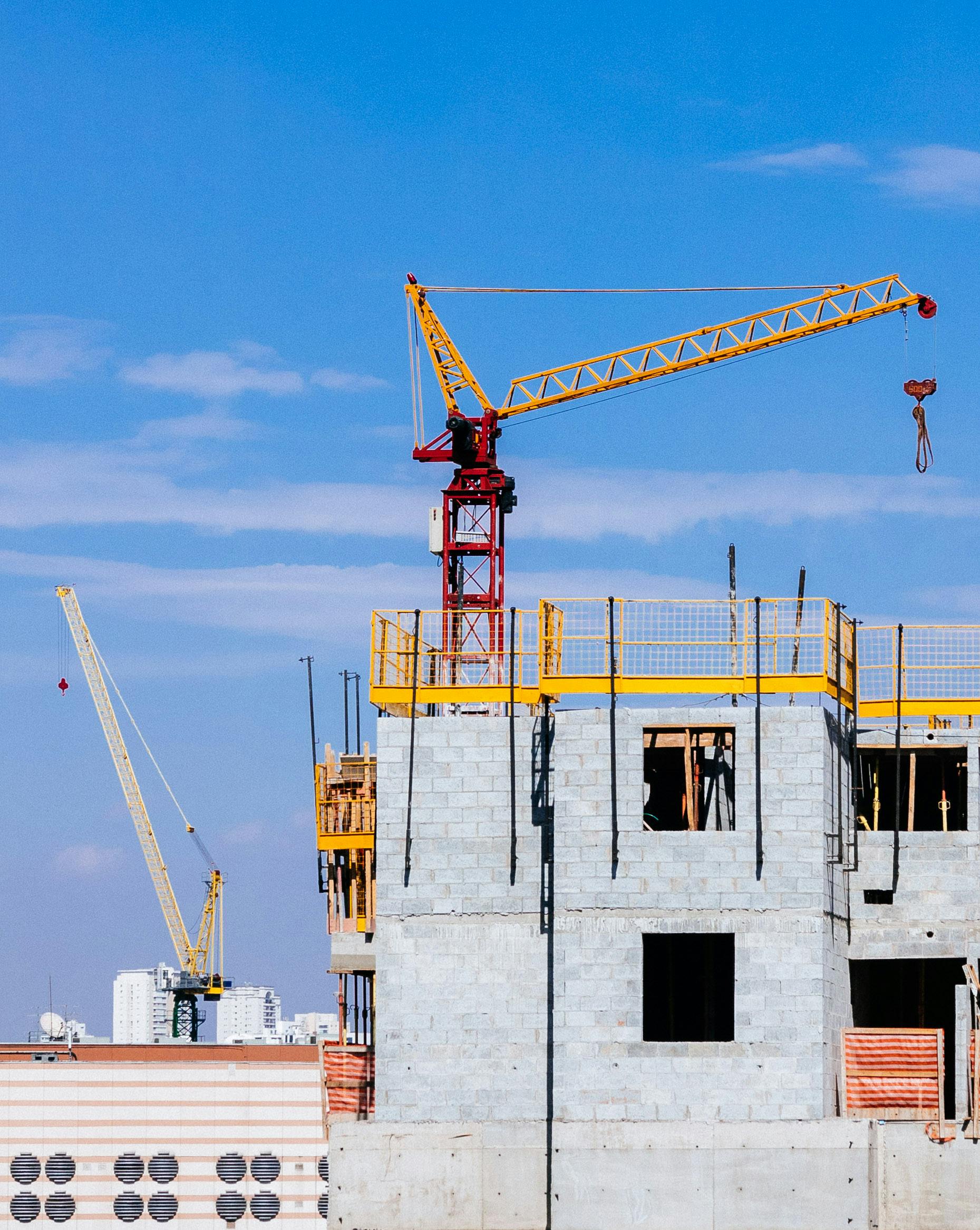 Tower cranes at a construction site working on a high-rise building under a clear blue sky.