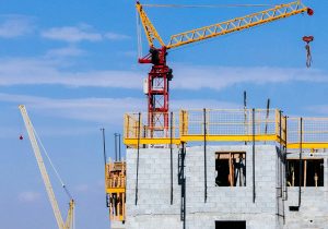 Tower cranes at a construction site working on a high-rise building under a clear blue sky.